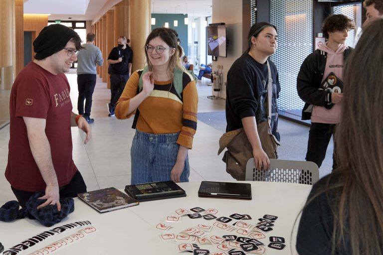 Students are gathered round a table with some tablets and stickers on it.