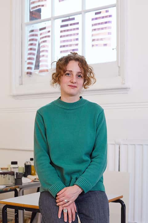 Staff portrait of Fine Art Lecturer Sophie Michael in a fine art studio, wearing a green chunky knit jumper