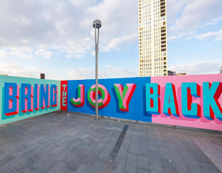 A photo of Rachel Joy Prices street art outside London Stratford shopping centre. The artwork says 'bring the joy back' in bright bold colours.