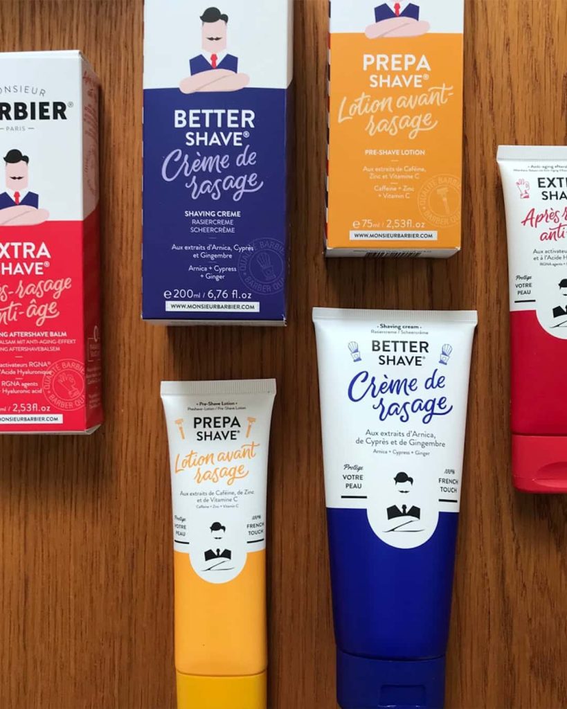 Monsieur Barbier products and packaging laid out on a wooden table. The packaging is brightly coloured with a small illustration of a male on the front.