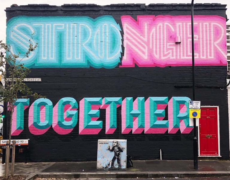 A photo of Rachel Joy Price and Ben Eine's graffiti on a London building. The artwork says 'stronger together' in blue and pink.