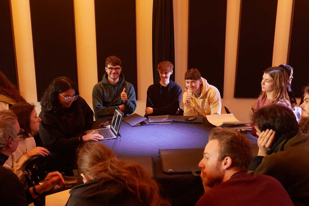 Students are seated around a round table. A purplish light illuminates the centre.