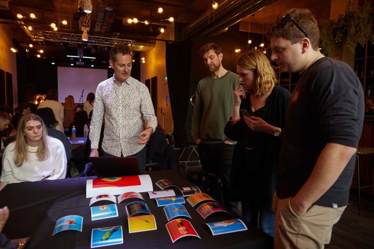 Tim Flach, Sam Christmas, Christine Harding and student Joey Rolph are stood round a table of Joey's images.