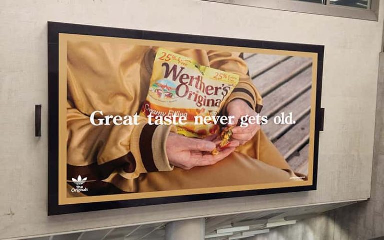 A digital mock-up of a billboard for a Werthers Original and Adidas campaign. The image is of a persons hands holding a packet of Werthers Original sweets whilst sitting down on a bench.