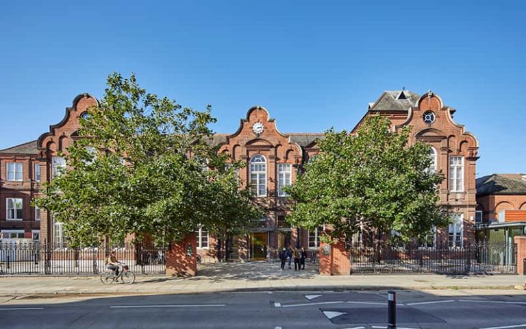 Duke Street building. Photograph of a red brick building with large windows with rounded tops. Two large, leafy trees stand either side of the entrance