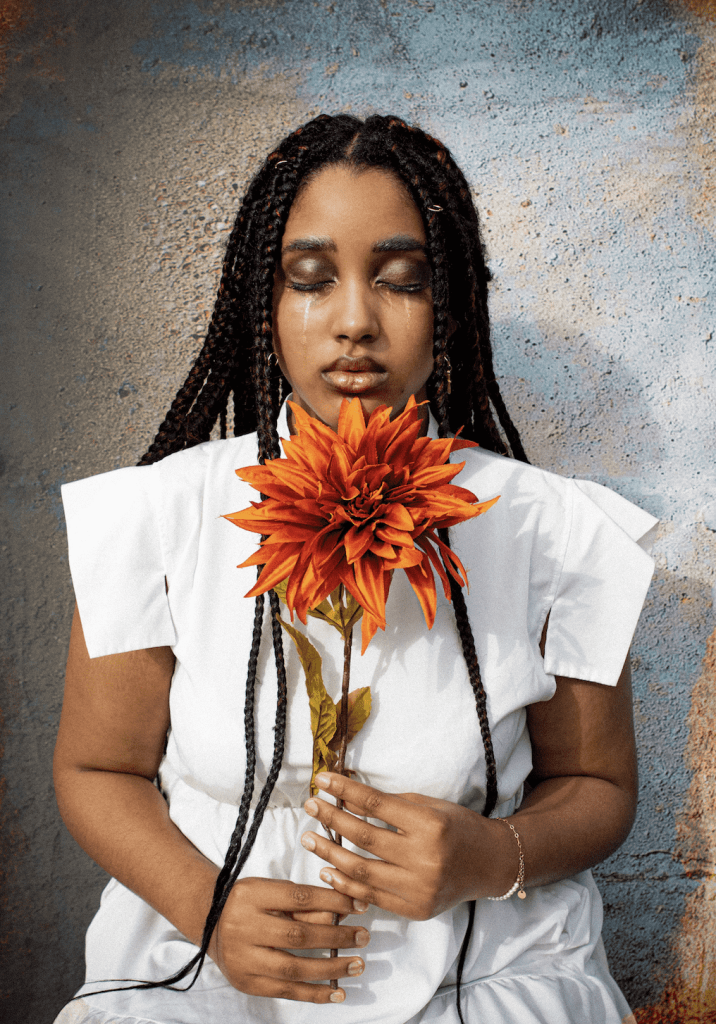 A photograph of a female holding a flower with her eyes closed and dressed in white.