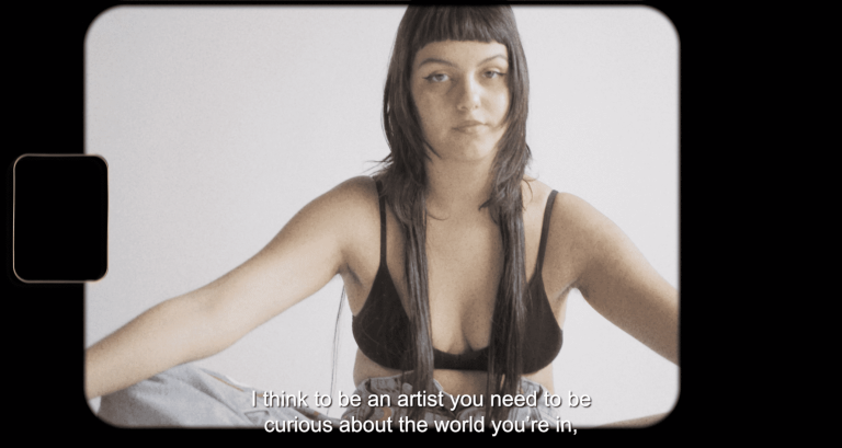 A portrait image of a female, sitting with her legs crossed wearing jeans and a crop top.