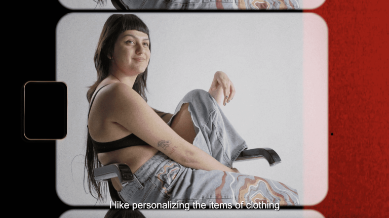 A photograph of a female sitting in a chair with her leg up on the seat, wearing a pair of jeans and a crop top.