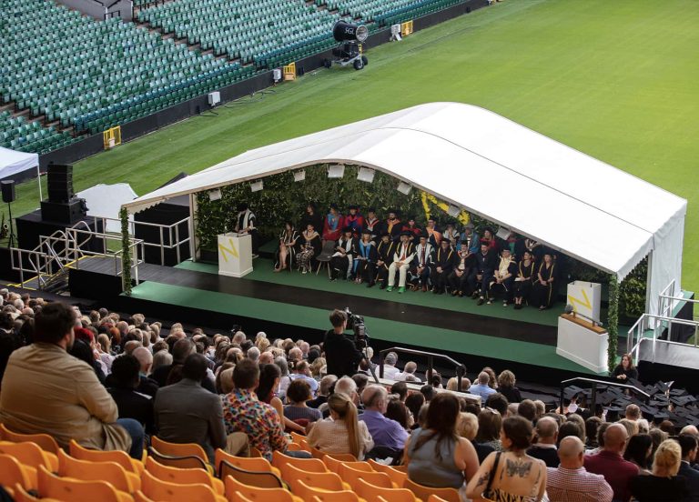 Norwich University of the Arts Graduation 2023 at Norwich city football stadium. A photo of the stage with a large number of people sat down, waiting for the ceremony to begin.