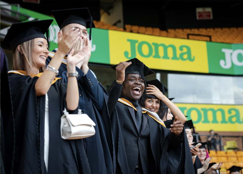 A photo of Norwich University of the Arts graduates smiling, waving and cheering at Graduation 2023.