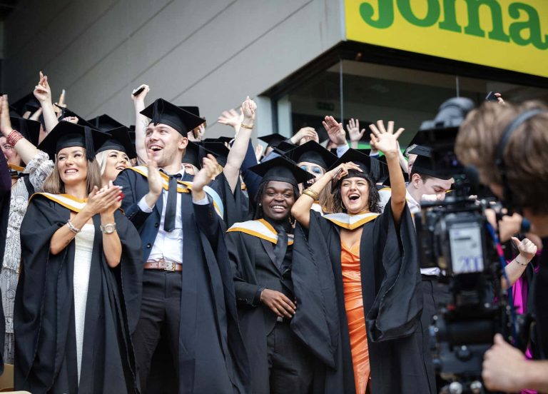 A photo of Norwich University of the Arts graduates smiling, waving and cheering at Graduation 2023.