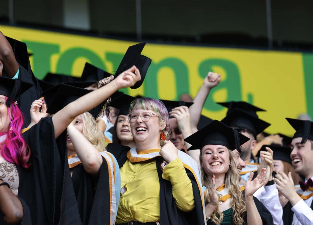 A photo of Norwich University of the Arts graduates smiling, waving and cheering at Graduation 2023.