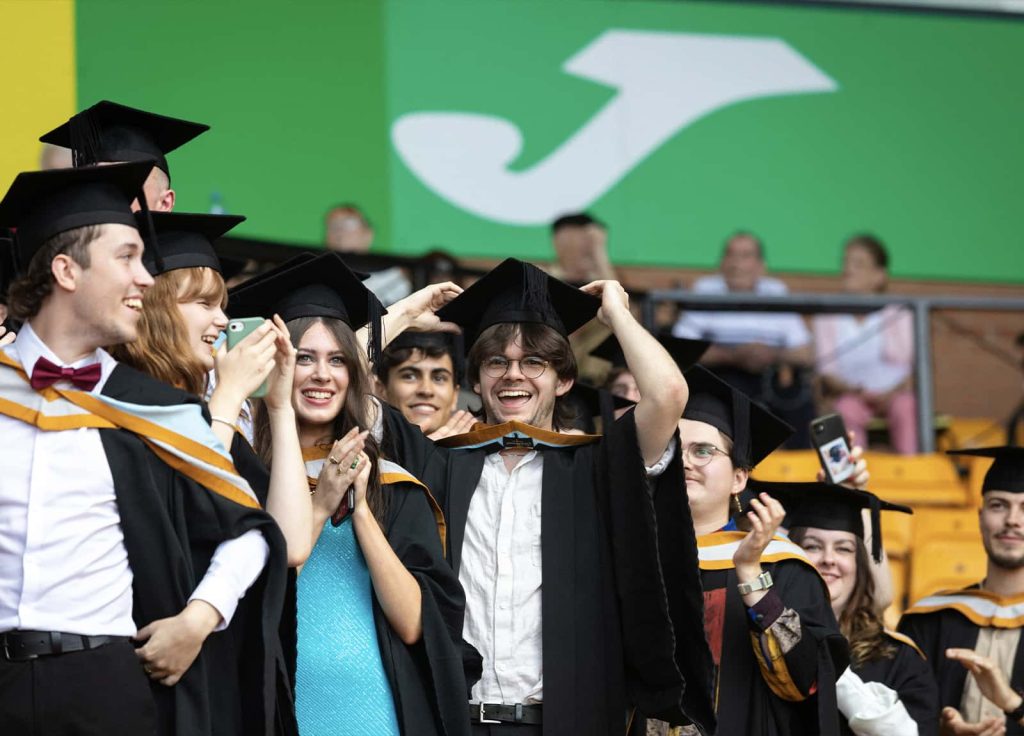 A photo of Norwich University of the Arts graduates smiling, waving and cheering at Graduation 2023.