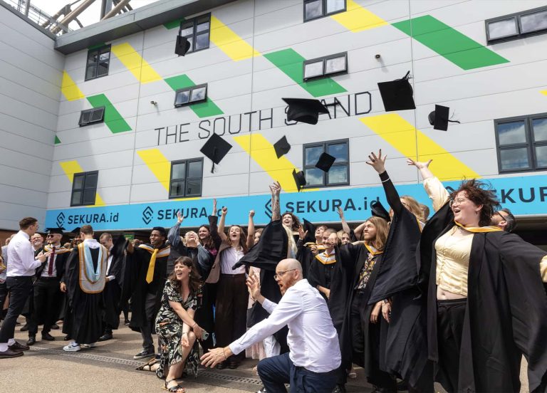 A photo of Norwich University of the Arts graduates celebrating and throwing their hats up in the air at Graduation 2023.