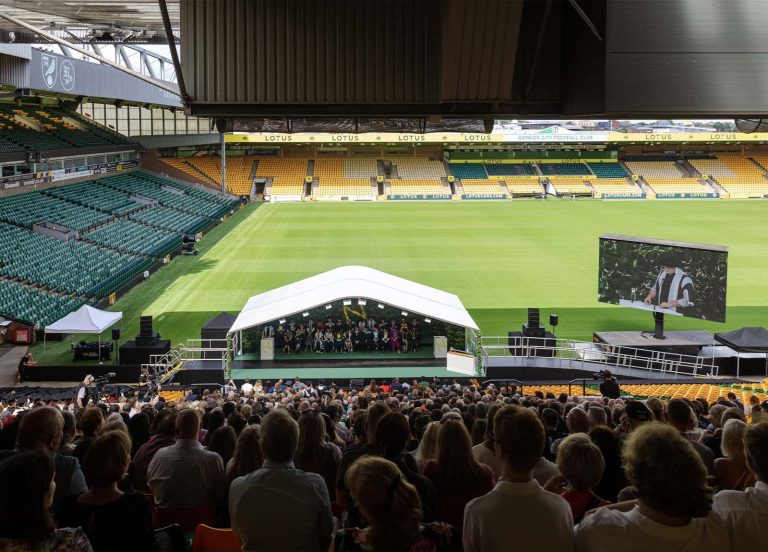 Norwich University of the Arts Graduation 2023 at Norwich city football stadium. A photo of the stage with a large number of people sat down, waiting for the ceremony to begin.