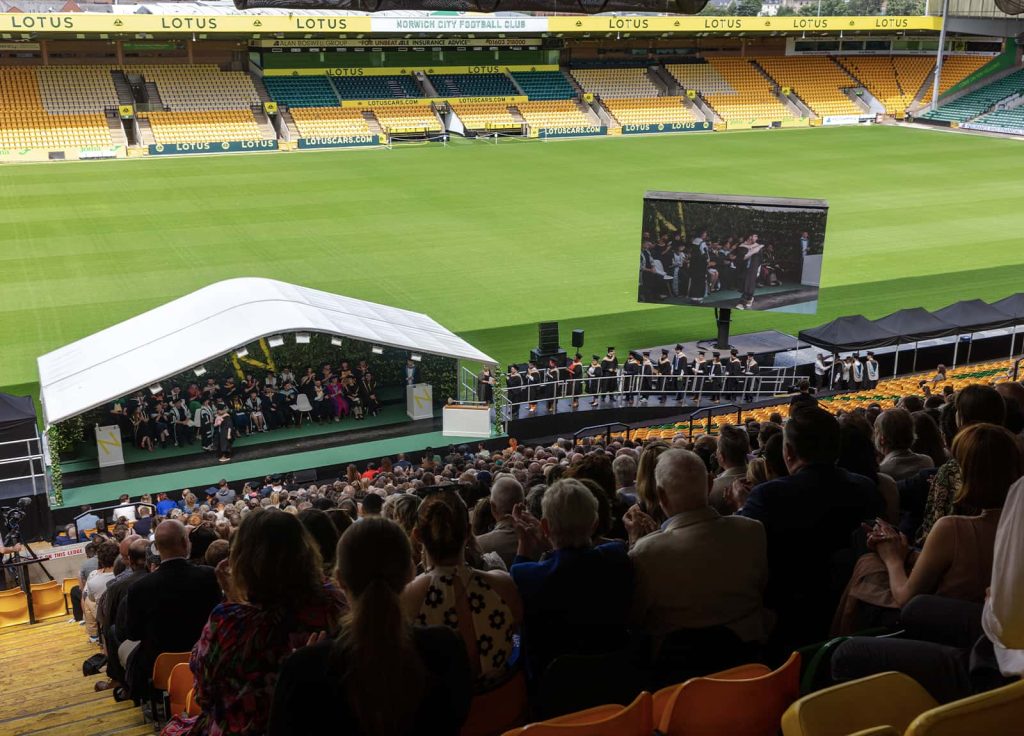 A photo of a stage with a large number of people sat down in-front of it at Graduation 2023.