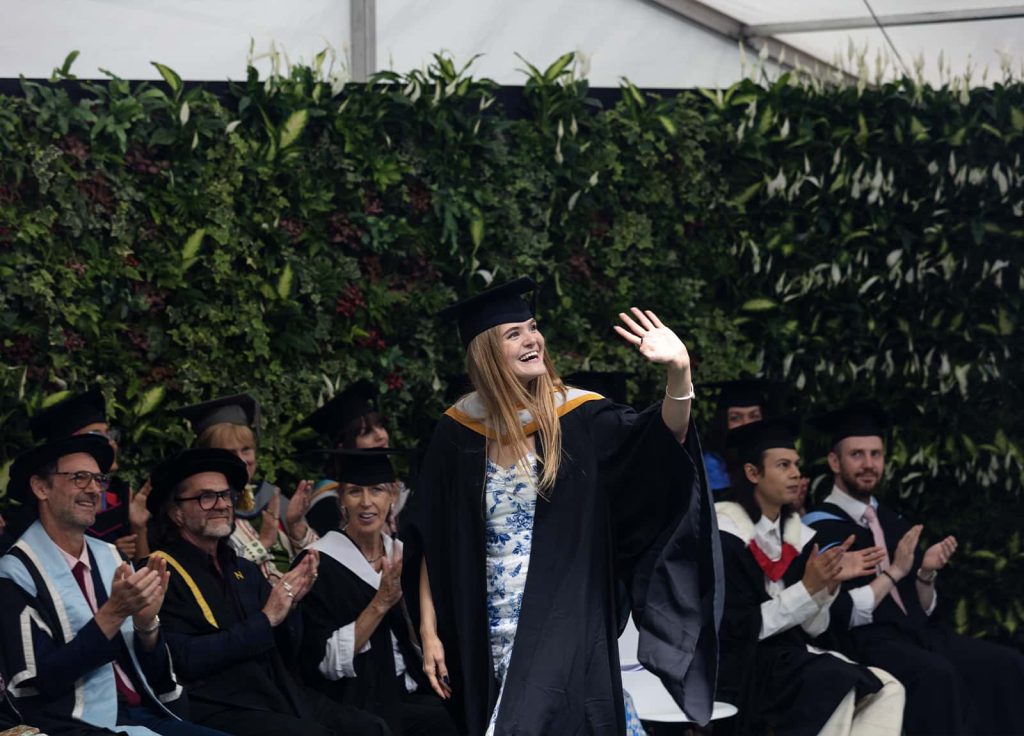 A photo of a student waving and walking across a stage at Graduation 2023.