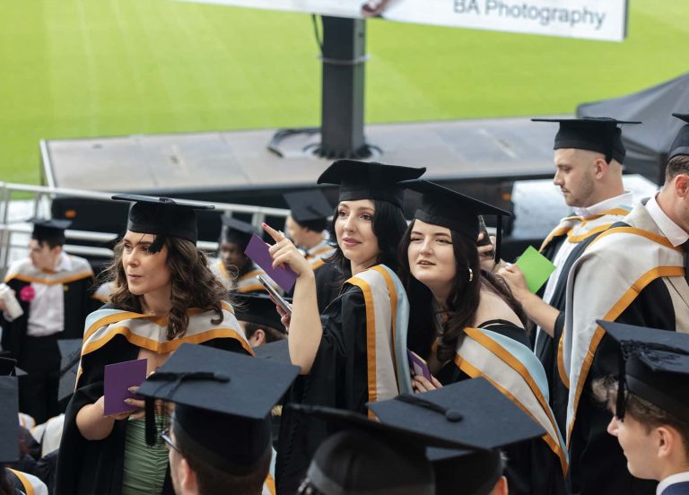 A photo of Norwich University of the Arts graduates pointing and looking in the direction to where their families were sat, at Gradation 2023.