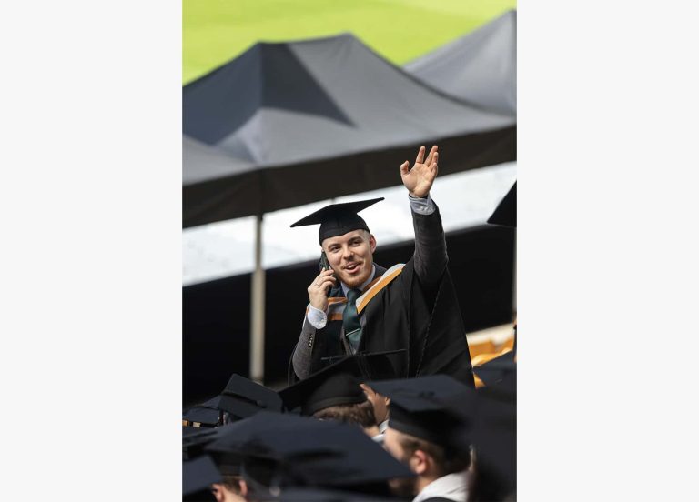 A photo of a Norwich University of the Arts graduate on the phone and waving their hand in the air.