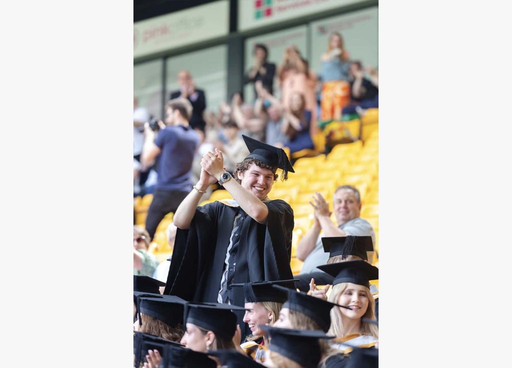 A photo of a Norwich University of the Arts graduate standing up and clapping their hands at Graduation 2023.