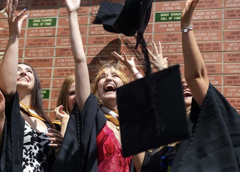 A photo of Norwich University of the Arts graduates celebrating and throwing their hats up in the air at Graduation 2023.