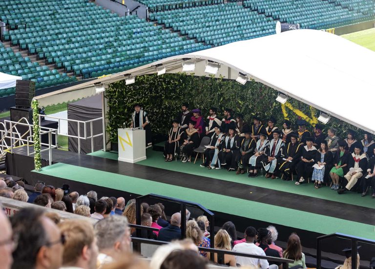 A photo of a stage with a large number of people sat down in-front of it at Graduation 2023.