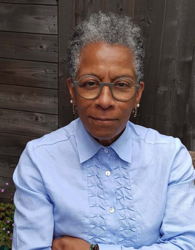 Profile of Ingrid Pollard wearing a blue shirt with arms crossed.