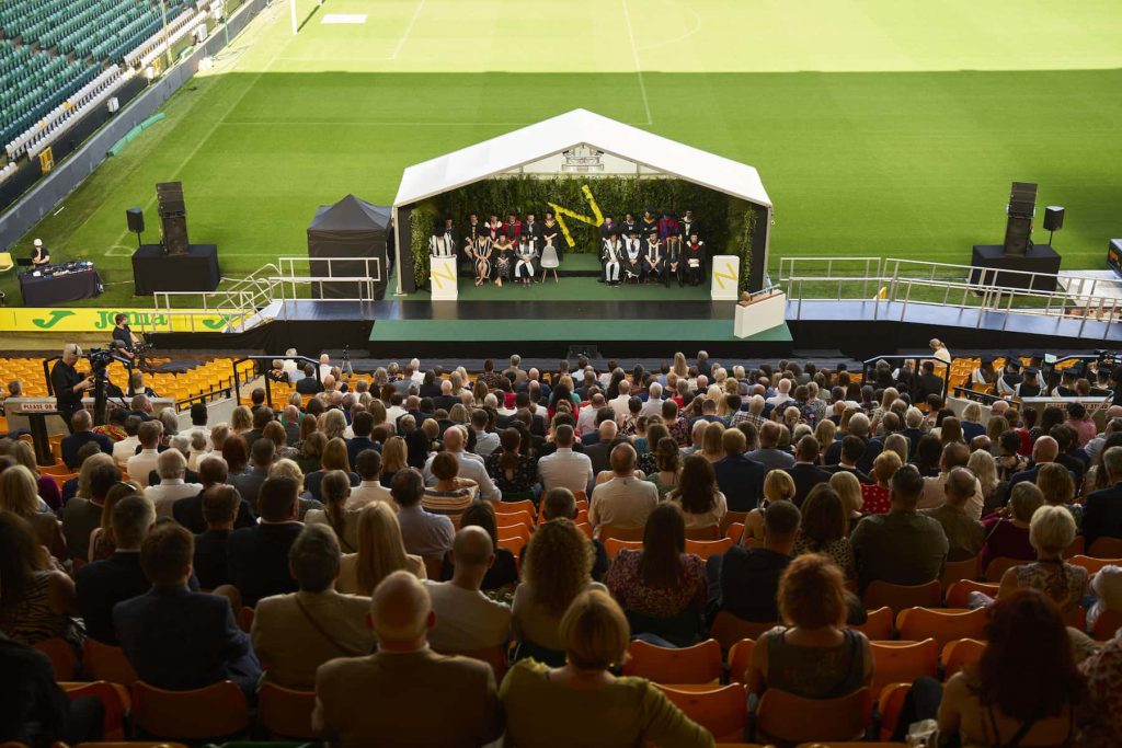 View of the Graduation stage at Carrow Road stadium with rows of guests in foreground.