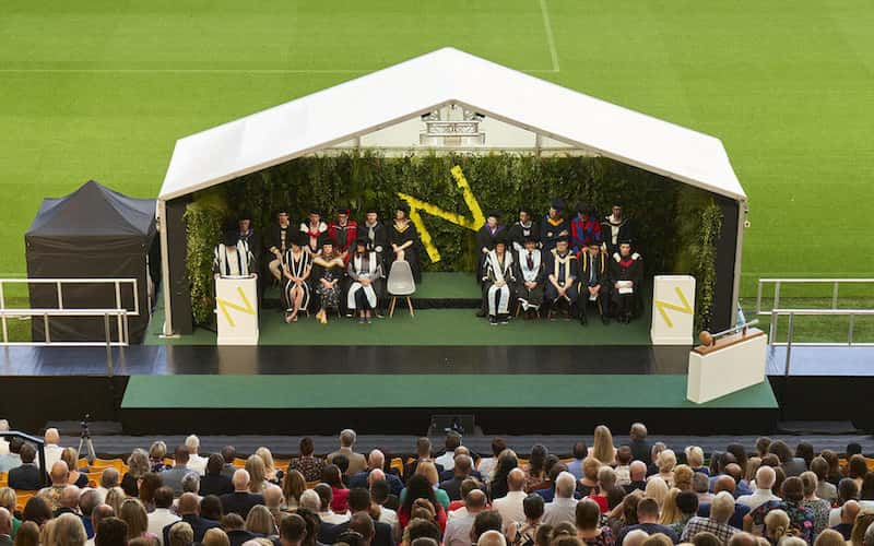 View of the Graduation stage at Carrow Road stadium with rows of guests in foreground.