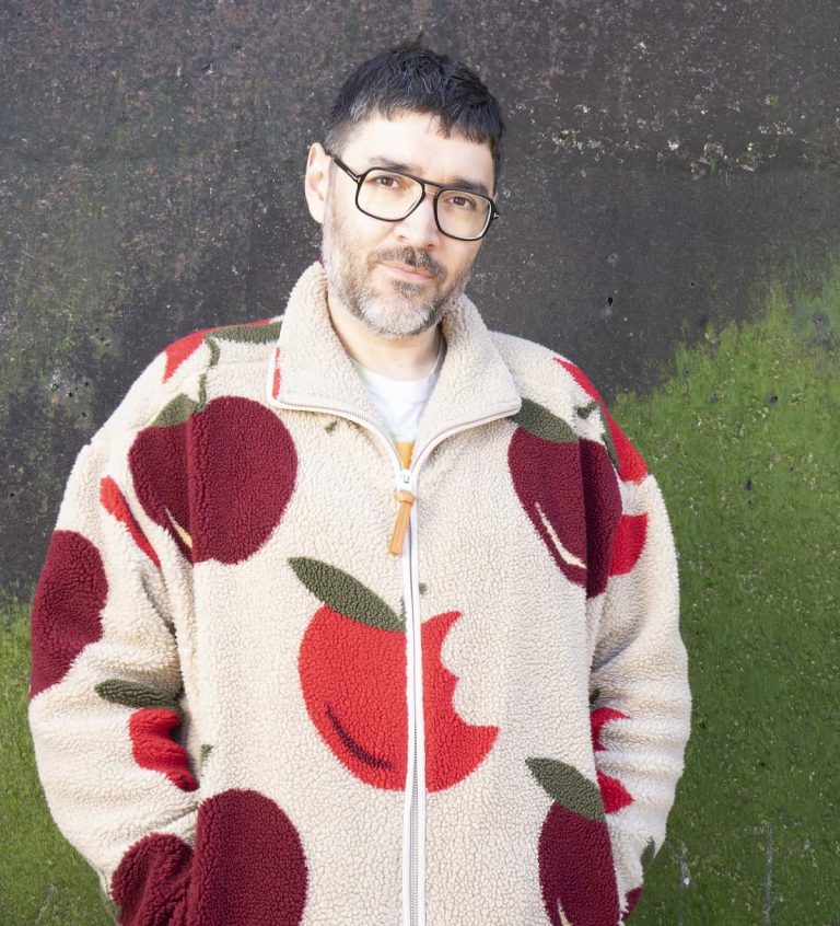 Robert Diament wearing an apple print jacket and glasses stood against a green wall.