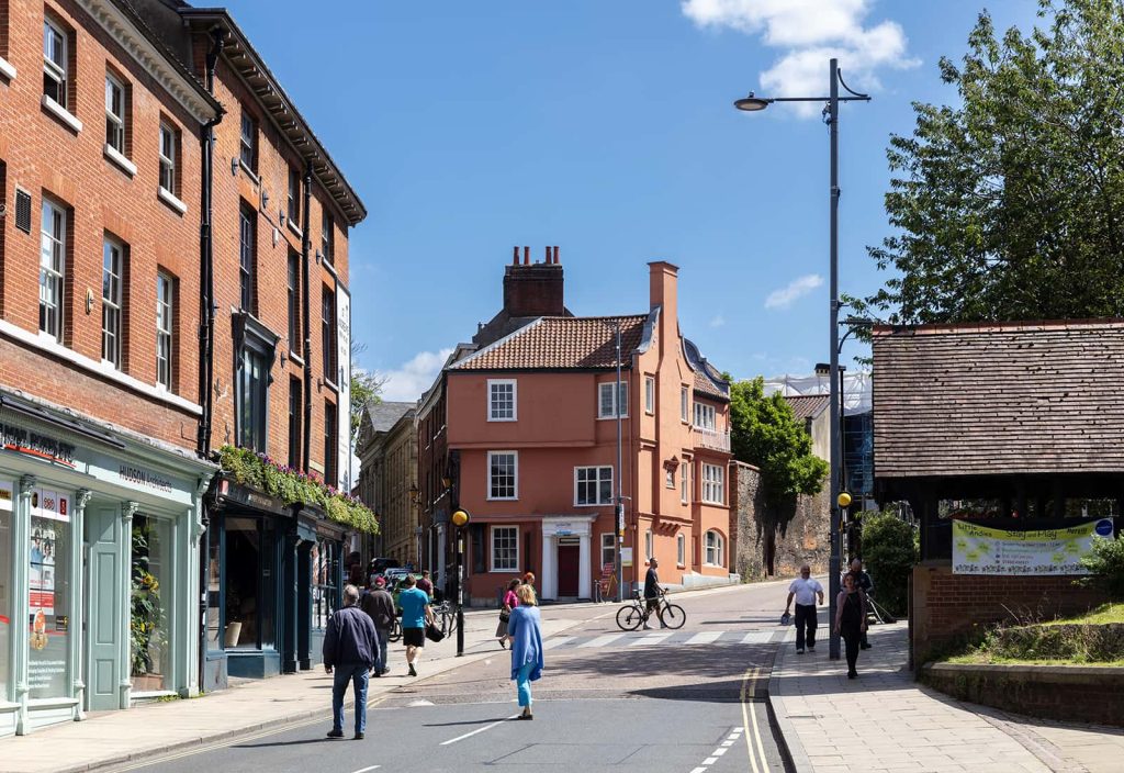 A photo of a road with people walking across it on a summers day.