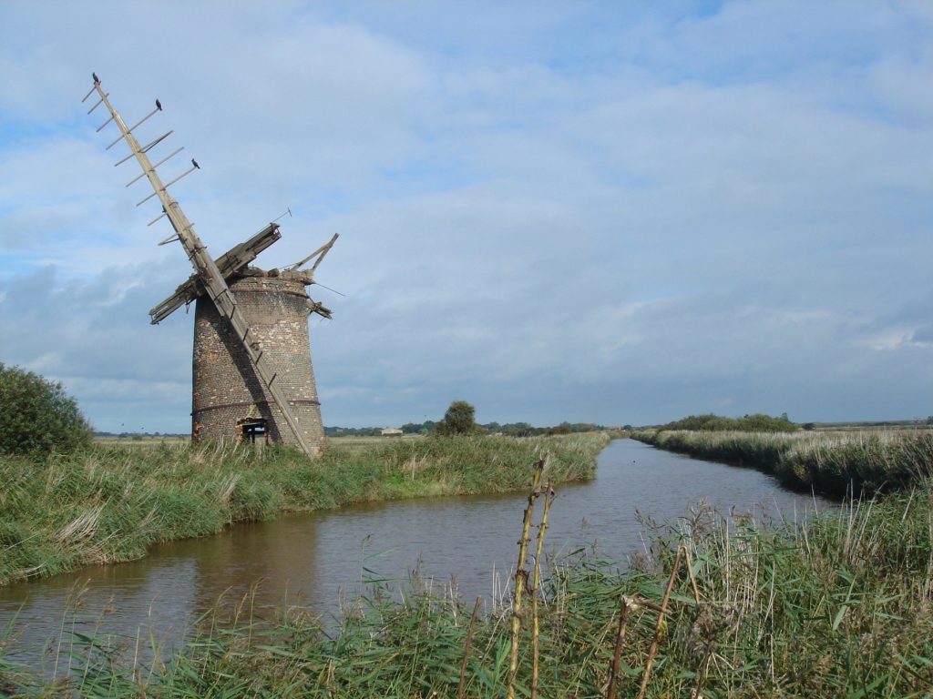 A disused windmill standing on the bans of a river in the Norfolk broads.