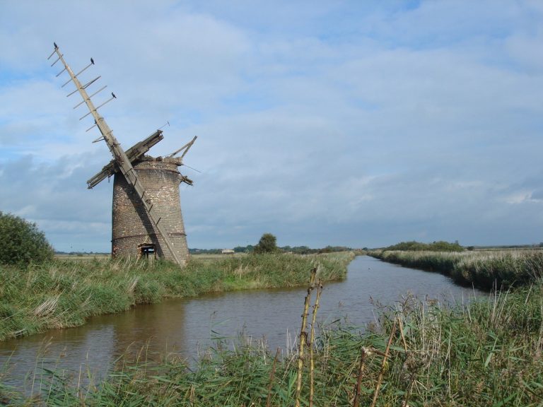 A disused windmill standing on the bans of a river in the Norfolk broads.