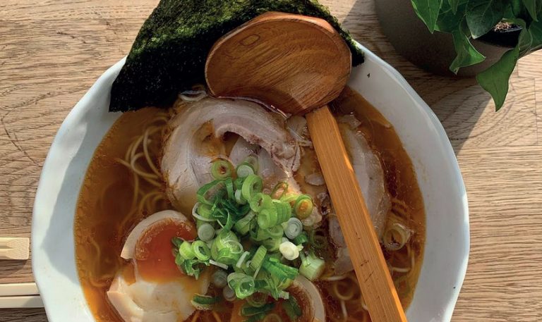 Top down shot of bowl of ramen from Soyokaze. A large wooden ladle is dipped into the bowl.