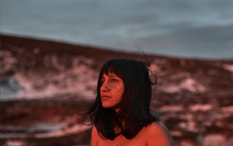 A woman with shoulder length black hair looks sadly over a barren horizon