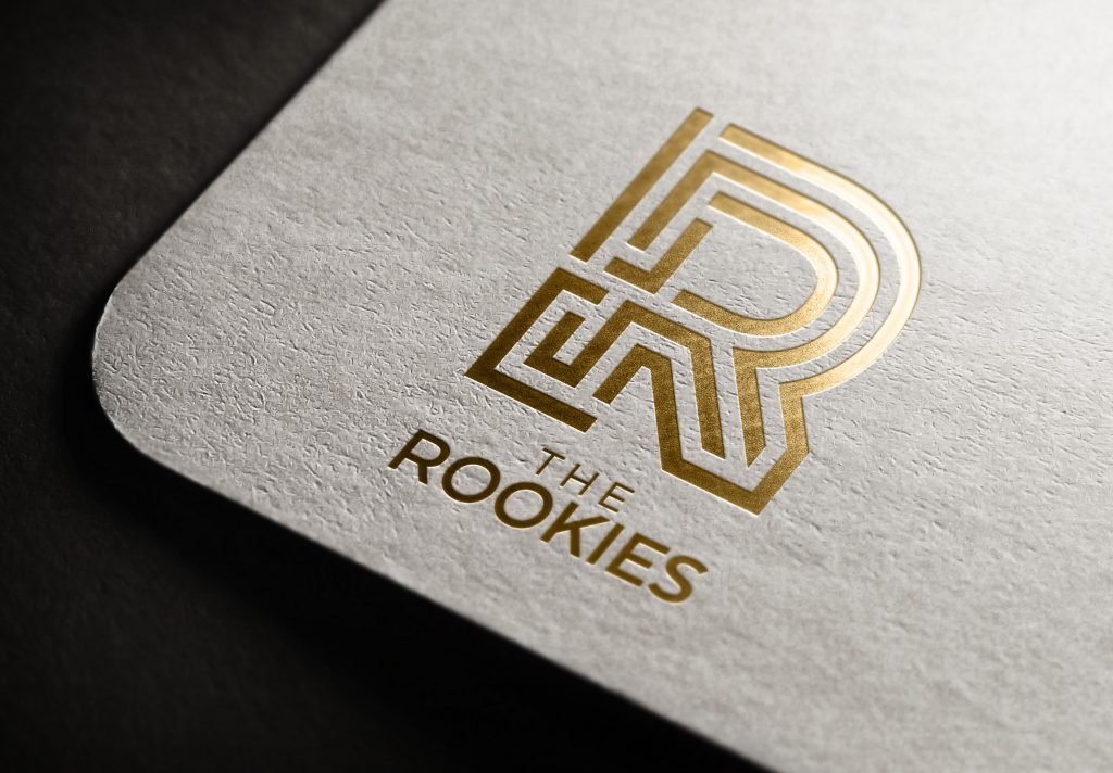The Rookies logo (a capital R) is embossed in gold onto the corner of a grey page.