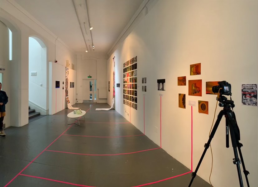 Photograph of an exhibition space, with a camera set on a tripod in the foreground.