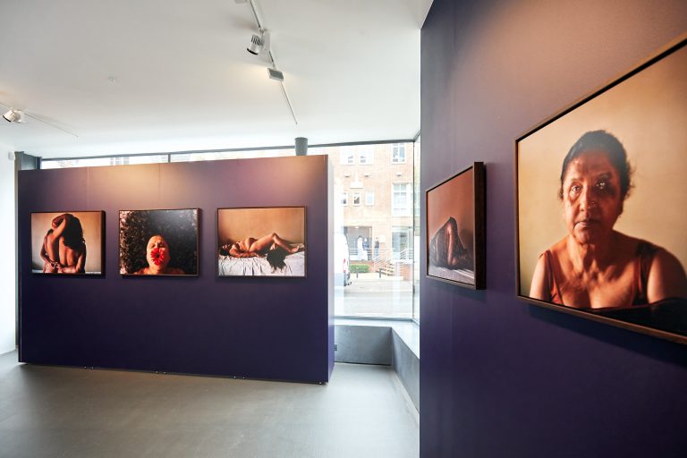 Interior photo of gallery - two purple screens have a variety of portrait photography hung on them.