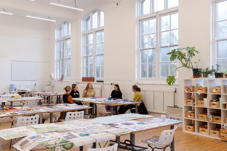 A photo of Textile Design students sat around a table with two Habitat designers discussing their work.