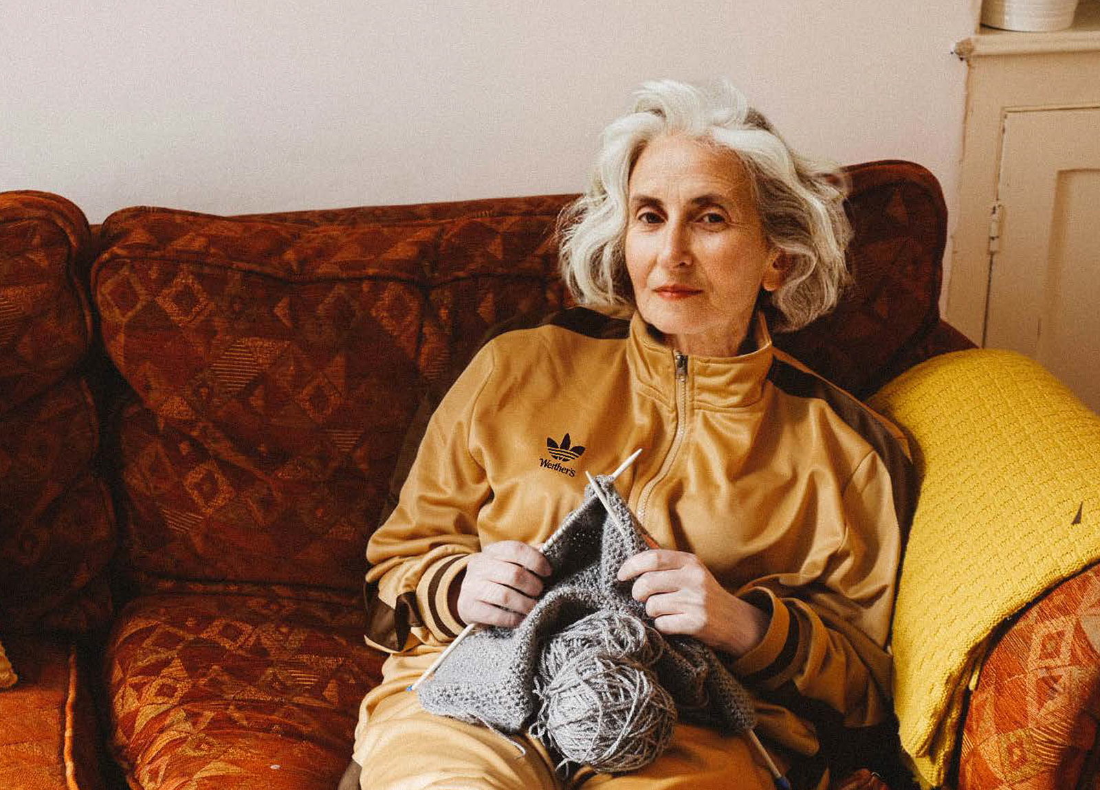 Student work by Eloise Woodcock-Jones, Reece Tenneson Parsons, and Olivia Knights. Image of an elegant elderly woman knitting, wearing a toffee coloured adidas tracksuit