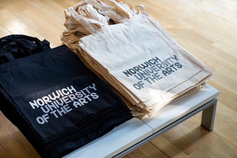 Norwich University of the Arts tote bags in piles on a table