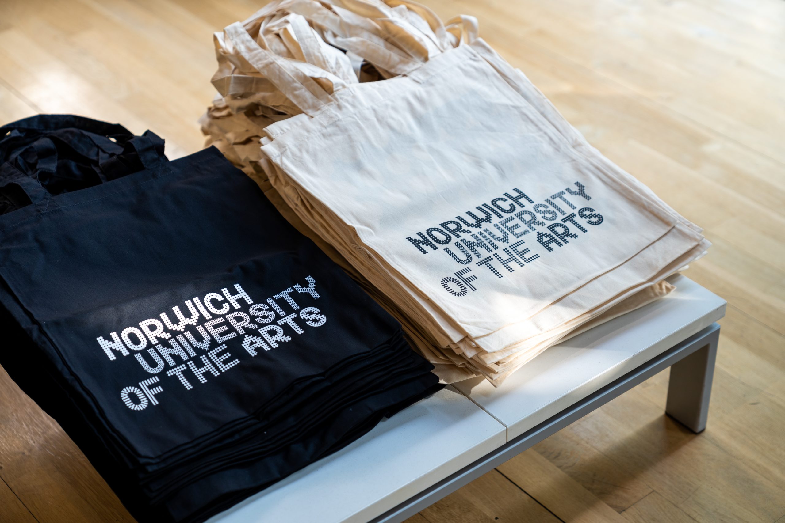 Norwich University of the Arts tote bags in piles on a table
