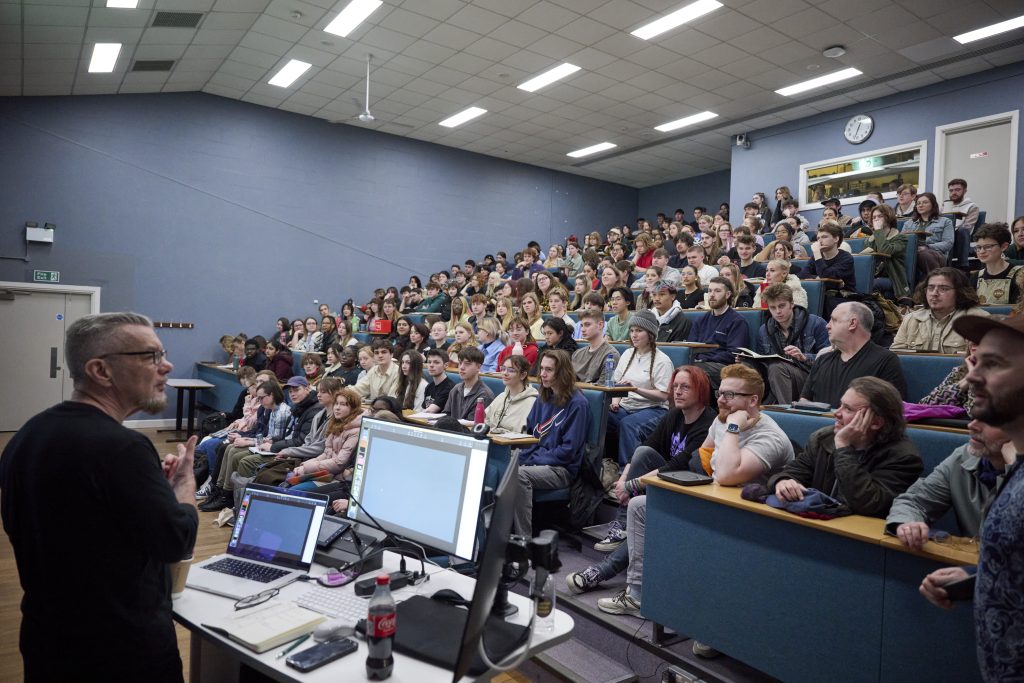 A photo of Neville Brody giving a lecture in Duke Street. The lecture theatre is full of students and staff.