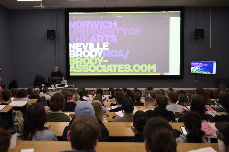 A photo of Neville Brody in Duke Street lecture theatre. The image shows a large group of people listening to his talk.