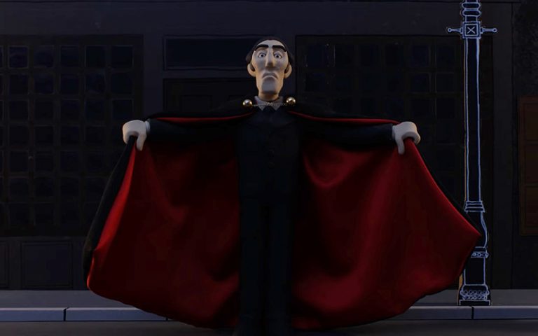 Still from claymation 'The Curse of Dracular'. A tall, pale man, Dracula, looks imposingly at the camera. He has arms outstretched holding his cape. He his dressed all in black, his cape has red lining.