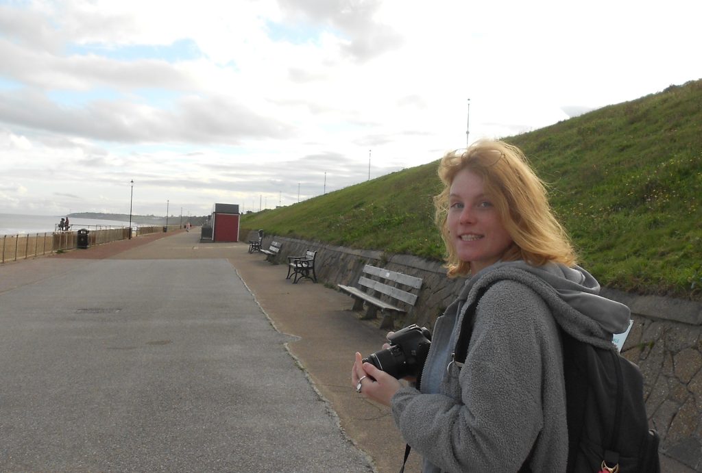 Student Monika Swiat walking along the seafront holding a camera.