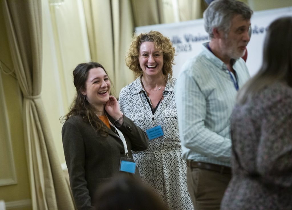 Student and colleague stood laughing wearing lanyards at an event.