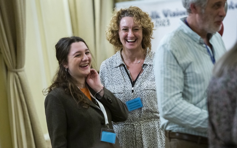 Student and colleague stood laughing wearing lanyards at an event.