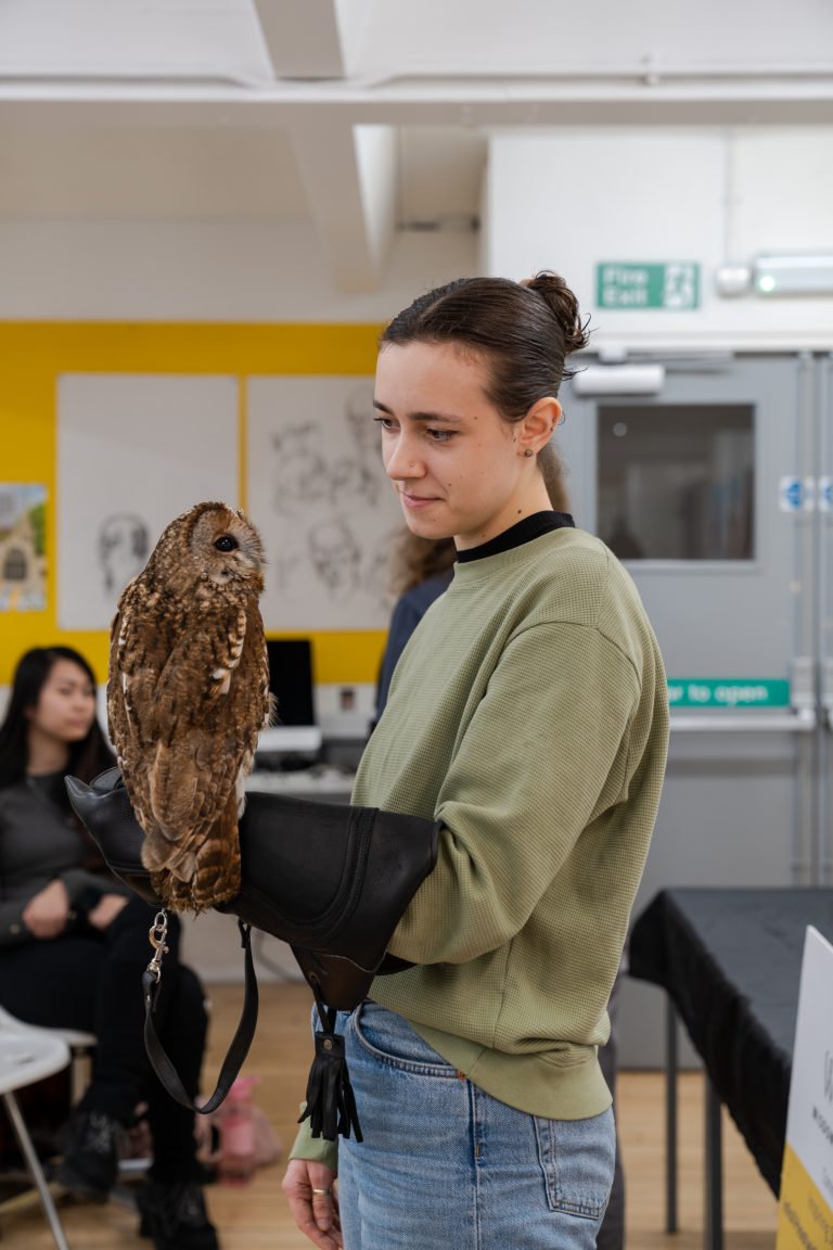 Photo of Indi holding an owl. Indi is wearing a green jumper.