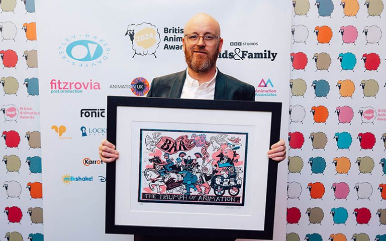 Jon Dunleavy holds a picture in a black frame. He is smiling to the camera, standing in front of a multi coloured board.